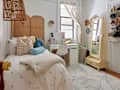 White bedroom with twin bed, natural room divider, rattan lamp, yellow floor mirror, vanity, and area rug.