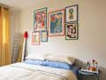 Cozy bedroom with a bed featuring blue and cream bedding, colorful wall art, a mirror, and a side table with decor.