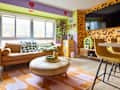 Colorful living room featuring a tan leather sofa, round coffee table, and vibrant decor with animal print walls.