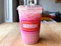 Iced pink beverage in a clear cup with a pink and orange Dunkin' logo, placed on a wooden table.