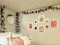 Dorm room with pale green walls, bed with pink and white bedding and throw pillows, faux pink roses and leaves hanging down walls, over bed, gallery wall by bed of pink and white art