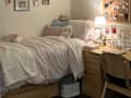 Cozy bedroom with a bed adorned in soft pink bedding, plush toys, and a wooden desk with decorative items and a lamp.
