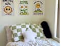 Cozy bed with green and white checkered pillows, a star-shaped pillow, and cheerful wall art featuring sun and flowers.