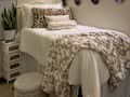Cozy bedroom with a white bedspread, leopard print pillows, a plush throw blanket, and a potted plant beside a nightstand.