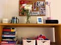 Desk shelf with two mugs, a vase of flowers, a pink lamp, JBL speaker, framed photo, and stacked books.