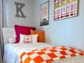 Cozy bedroom with a white bed, colorful pillows, and wall art featuring a car and "Rocky Top" sign.