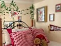 Cozy bedroom with a bed featuring red gingham pillows, stuffed animals, and ivy decor on the walls.