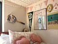 Cozy bedroom with a floral comforter, heart-shaped pillows, and wall decor including a tennis racket and posters.
