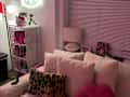 Cozy living room corner with a plush white sofa, leopard print pillow, pink lip-shaped cushion, and a Hello Kitty neon sign.