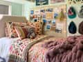 Cozy bedroom with a floral quilt, colorful pillows, a stuffed sloth, and a wall collage of photos and hats.