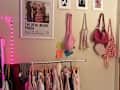 Clothing rack with various garments in soft colors, framed movie poster, and fashion magazine prints on the wall.