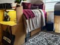 Cozy dorm room with a lofted bed, purple bedding, a desk with a microwave, and a leopard print rug.