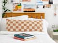 closeup shot of books on a bed with checkered orange and cream pillow behind it - photo gallery wall behind headboard