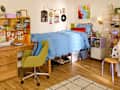 Cozy bedroom featuring a blue ruffled bedspread, a green swivel chair, a wooden desk with decor, and a bookshelf.