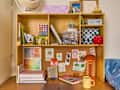 A wooden desk organizer filled with art supplies, photos, and decor, featuring a colorful lamp and a yellow mug.
