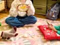 A cozy indoor scene with three people crafting on a colorful rug, holding yarn, scissors, and a phone.
