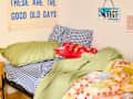 Cozy bed with blue checkered pillows, green bedding, colorful quilt, and a decorative red pillow with patterns.