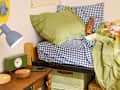 Cozy bed with green and blue checkered bedding, a wooden nightstand, a green clock, and a lamp.