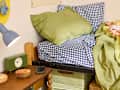 Cozy bed with blue and white checkered bedding, green pillows, a green clock, and a wooden nightstand.