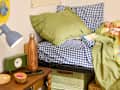 Cozy bed with green and blue checkered bedding, wooden nightstand, lamp, water bottle, and a smartphone.