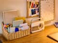 Desk with a woven basket of colorful stationery, a vintage radio, and a calendar for April on the wall.