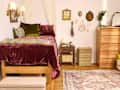 Cozy bedroom with a lofted bed, burgundy bedding, decorative pillows, wooden dresser, and wall art.