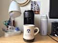 Coffee mug with "Columbia University" logo on a desk next to a Keurig coffee maker, lamp, and water bottle.
