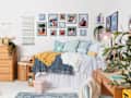 Cozy bedroom featuring a bed with colorful pillows, a wooden dresser, framed photos on the wall, and a pink lamp.