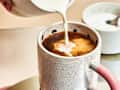 Someone pouring cream into coffee in a ceramic mug