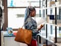 A black female student in her 20's standing looking through books in the library.