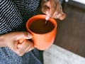 view of woman's hands stirring coffee in an orange mug. rug and wood floor visible below.