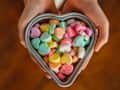 Hands holding a heart-shaped dish of conversation hearts candy