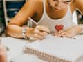 Young woman concentrated as she write in a ruled notebook, possibly for planning, journaling, or note-taking.
