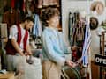Man and woman exploring a vintage clothing store filled with unique items and accessories. Man examining items on rack, woman holding a shirt with focus on details