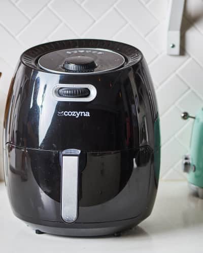 Cozyna air fryer on a kitchen counter with wooden utensils and a green toaster.