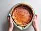 someone is holding basque cheesecake in a glass bowl out of the oven