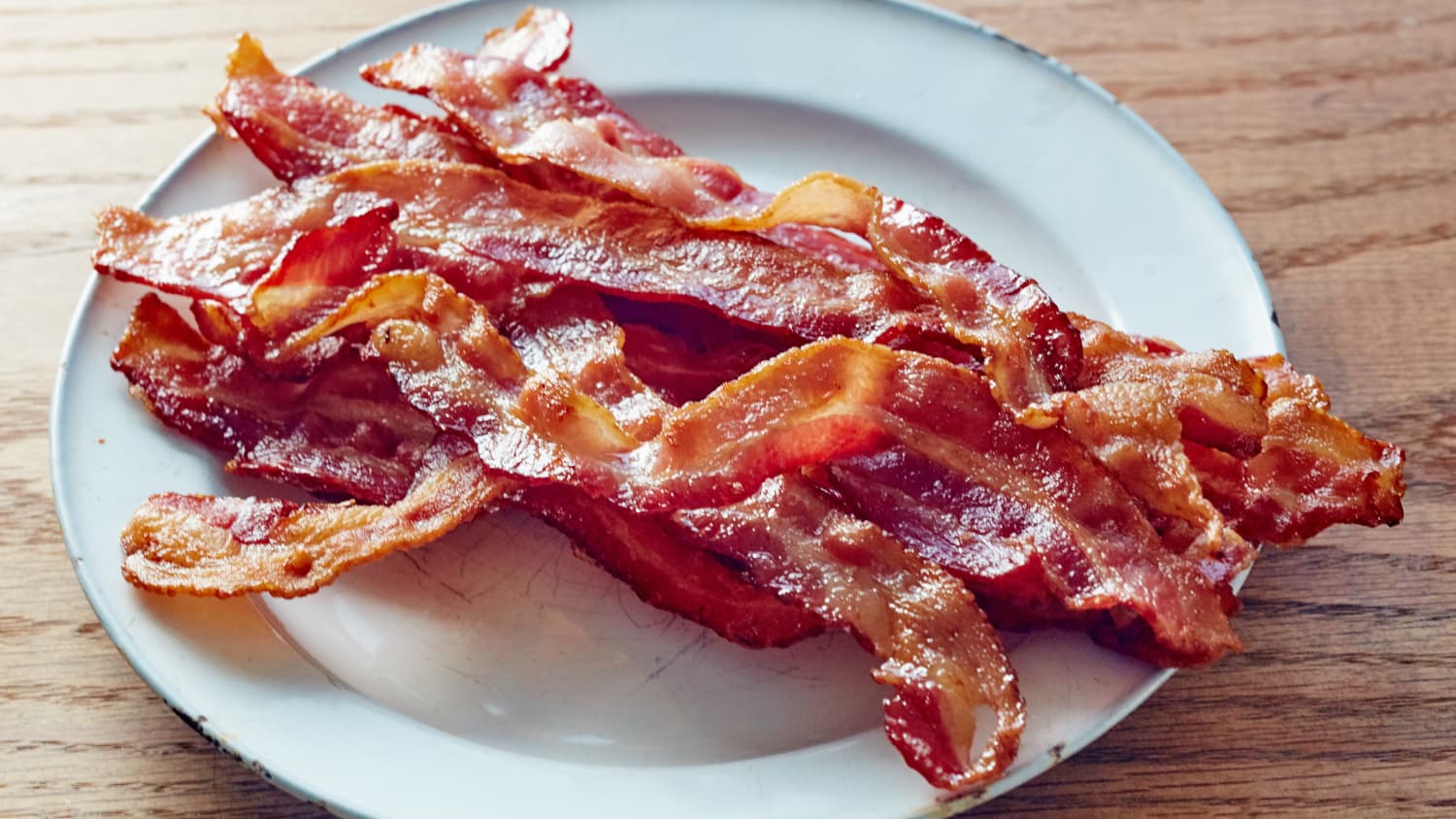 Frying pan with fried eggs and bacon on stove with fresh fruit and vegs  near by