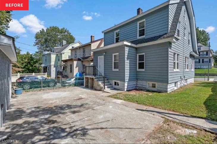 Empty concrete area between garage and blue house with side lawn.