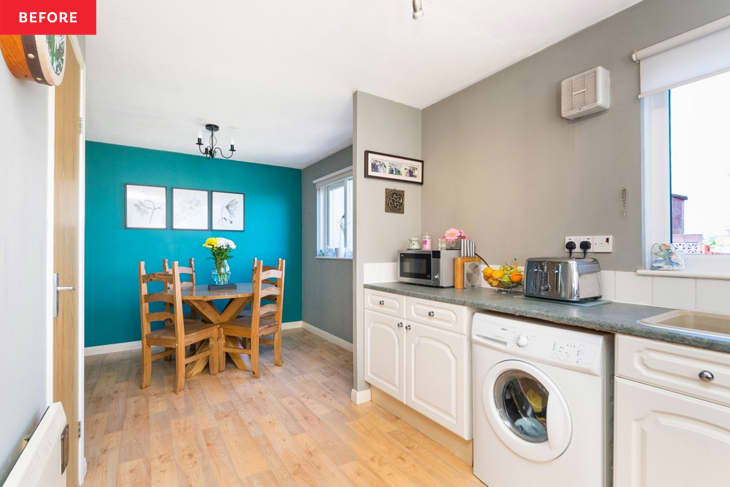 Wood dining table and chairs in turquoise room seen from gray kitchen with white cabinetry.