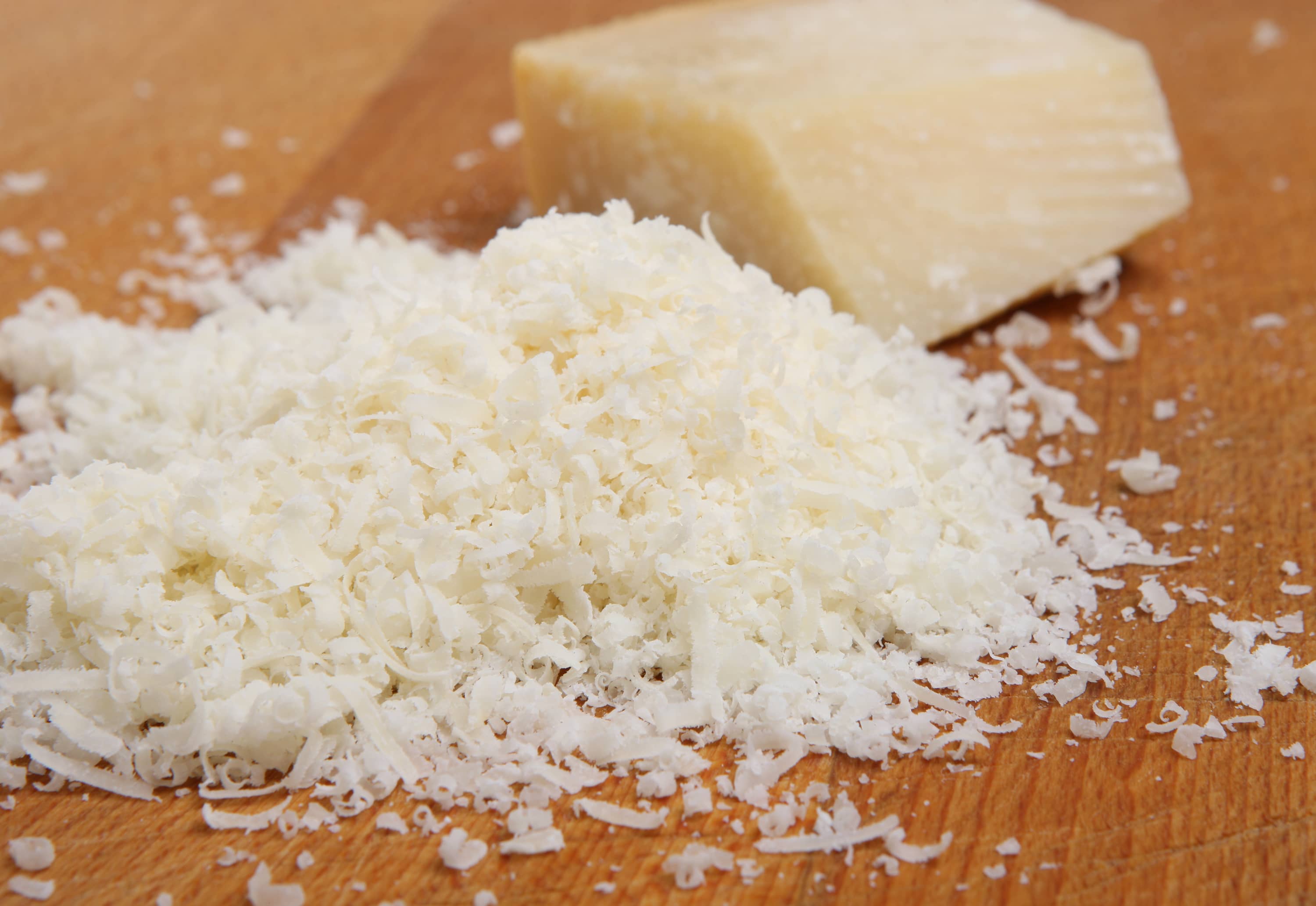 Parmesan Cheese and Grater Medium. an wider view of a block wedge of  parmesan cheese with shredded pieces all around and a metal cheese grater  on a cutting board Stock Photo