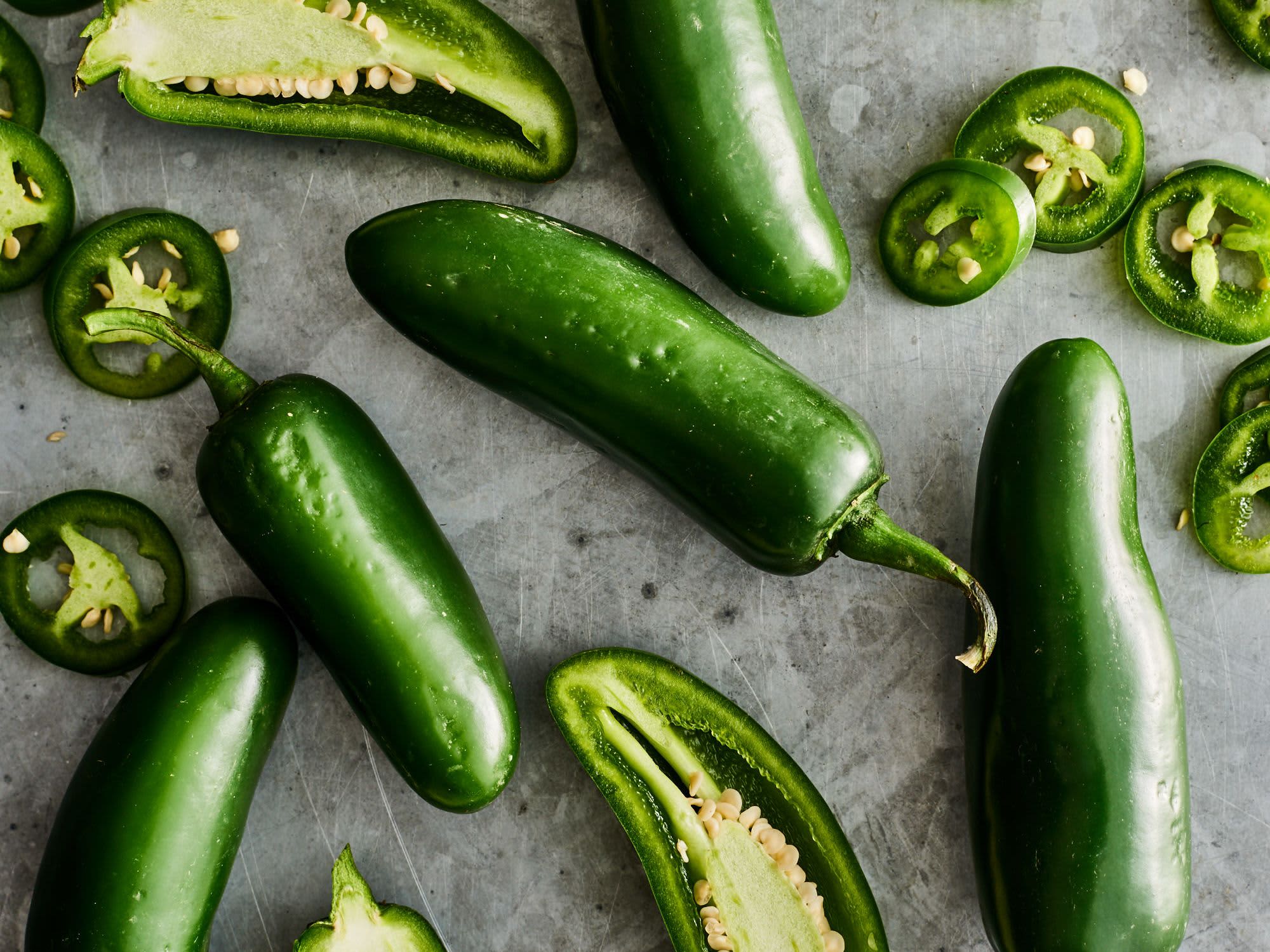 Top-down view of fresh jalapeño peppers, whole and sliced, showing seeds.